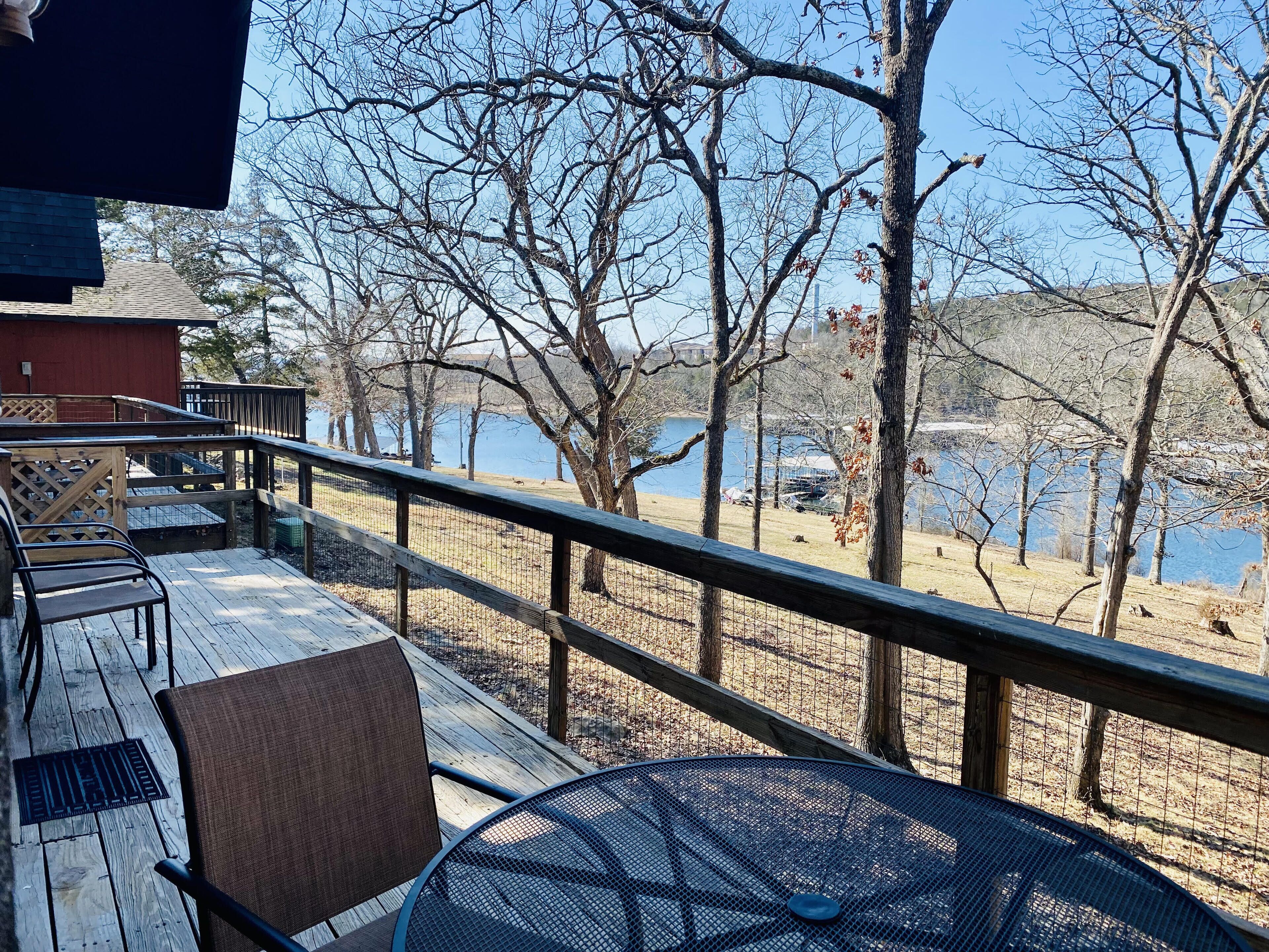 A wooden deck with outdoor seating, overlooking a lake and trees.