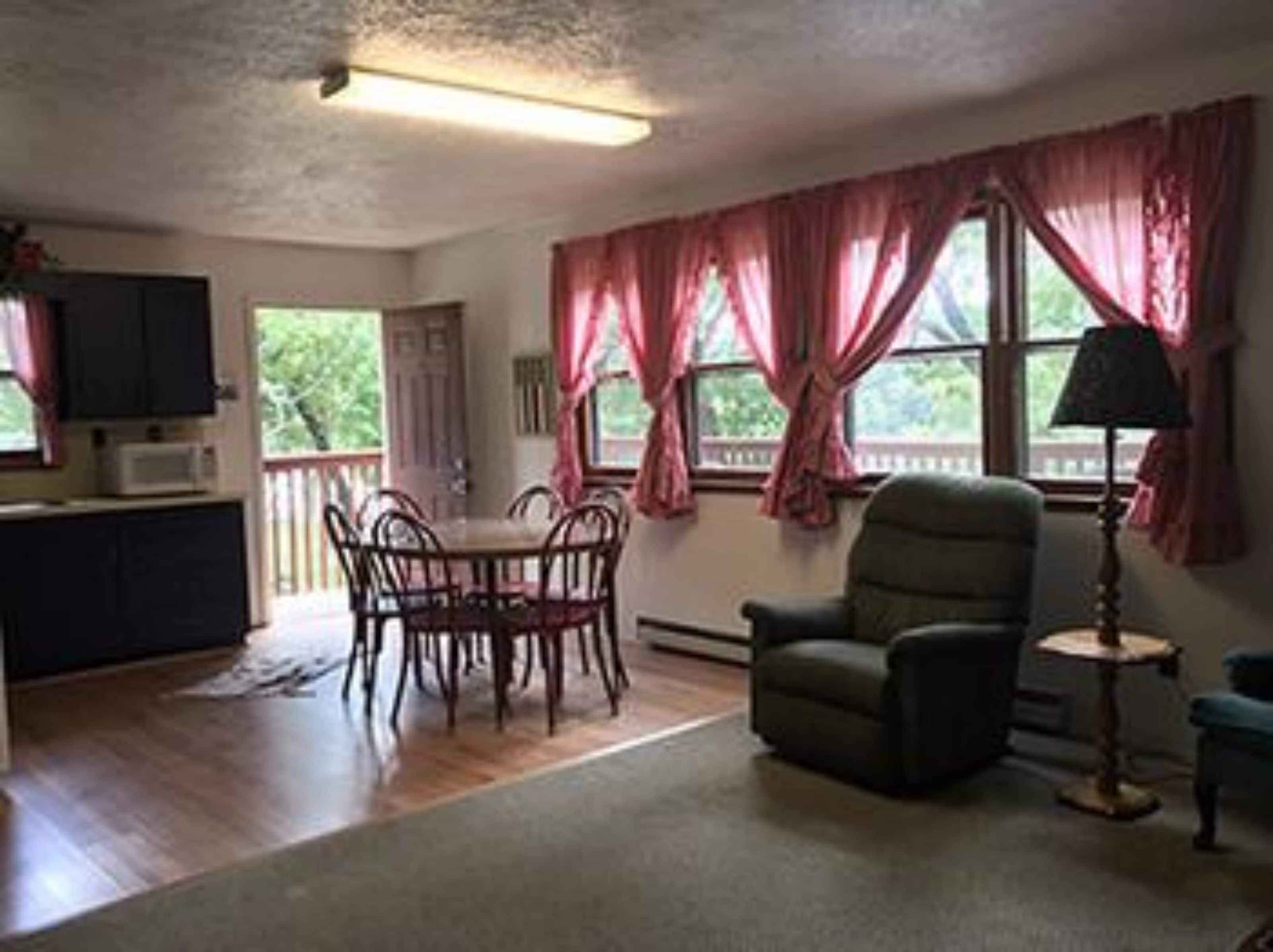 Ein Zimmer mit Esstisch, Stühlen, einer Couch, einer Lampe und einem Fenster mit Vorhängen.