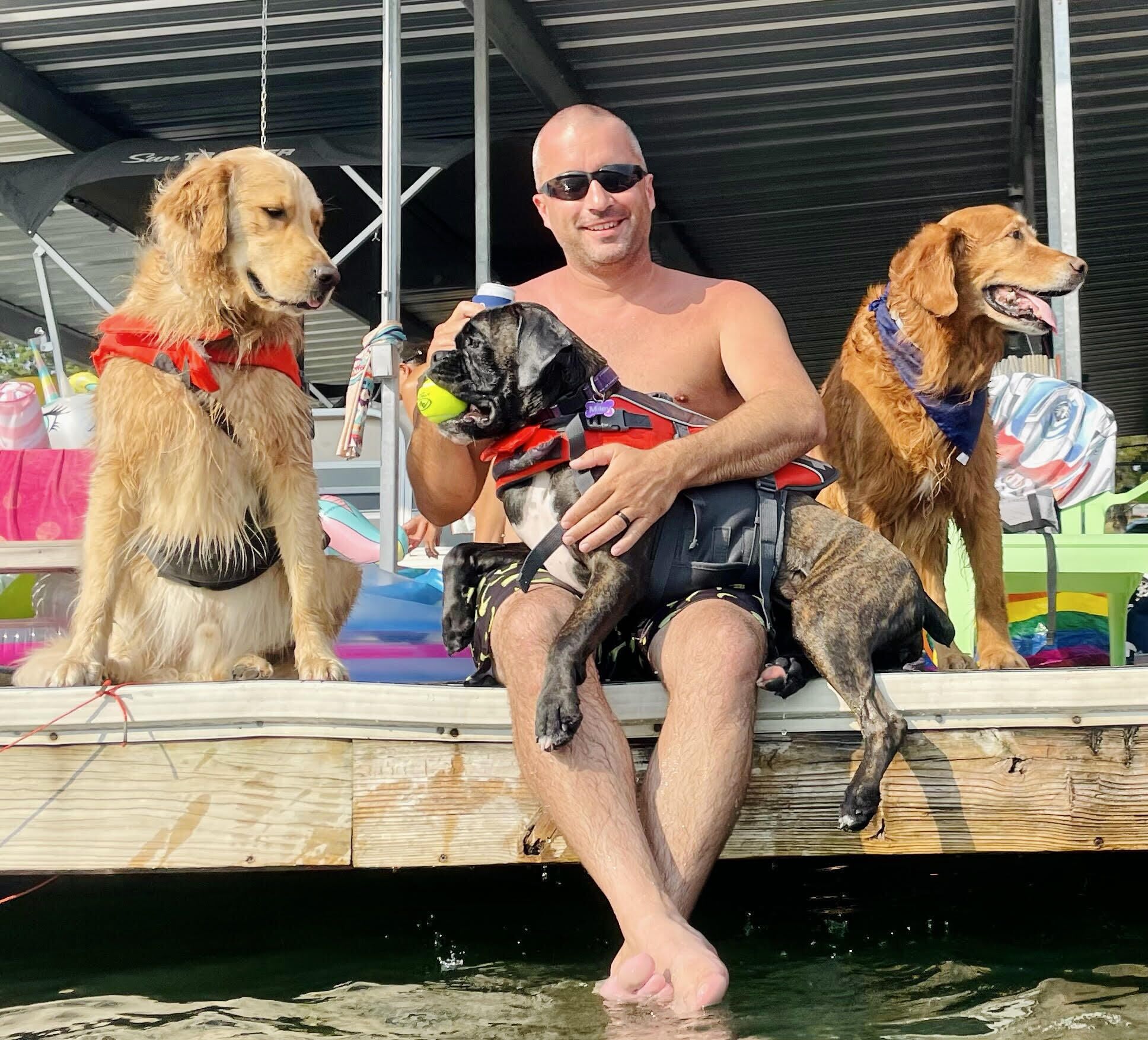 A person sitting on a dock with two dogs, one on each side.