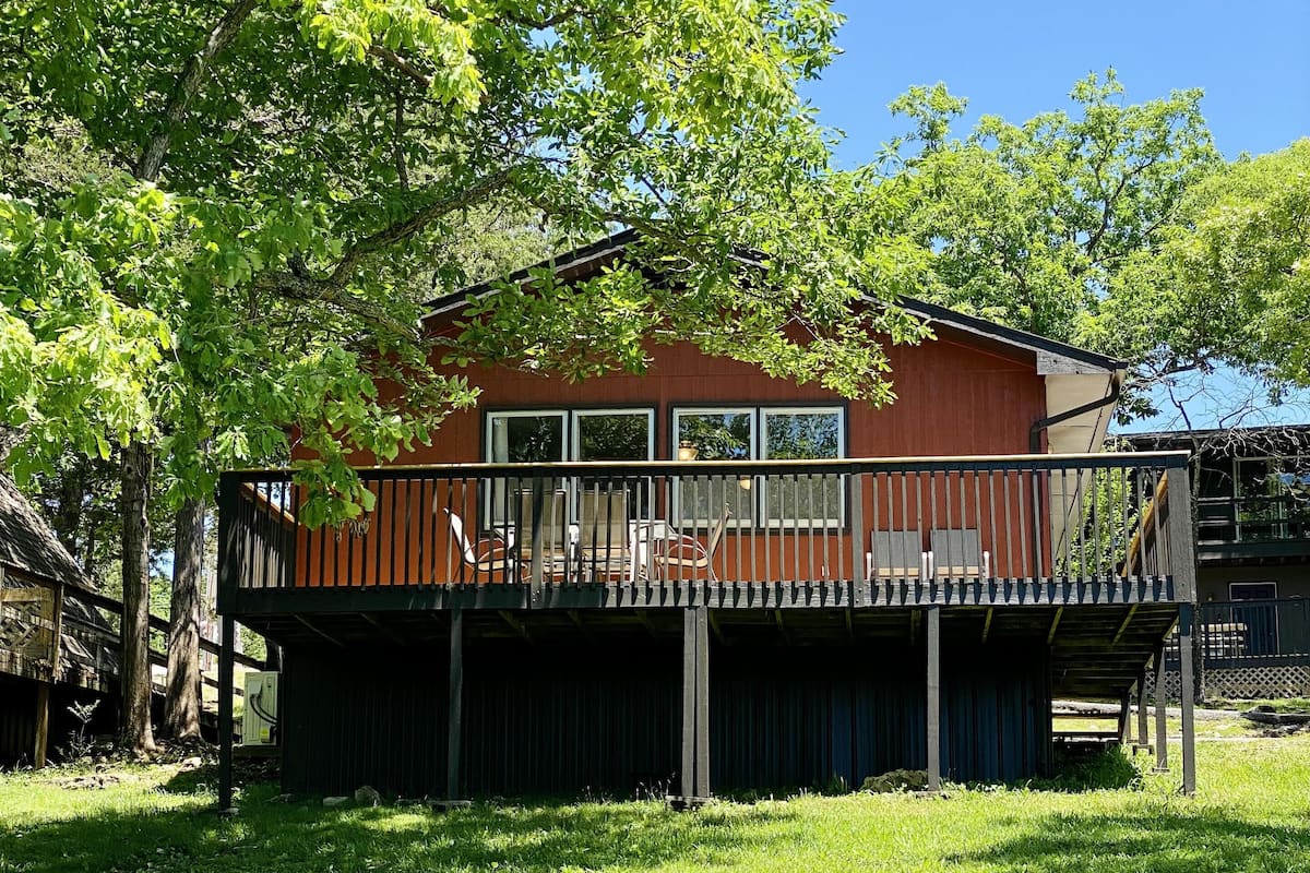 A two-story house with a deck, surrounded by trees and grass.