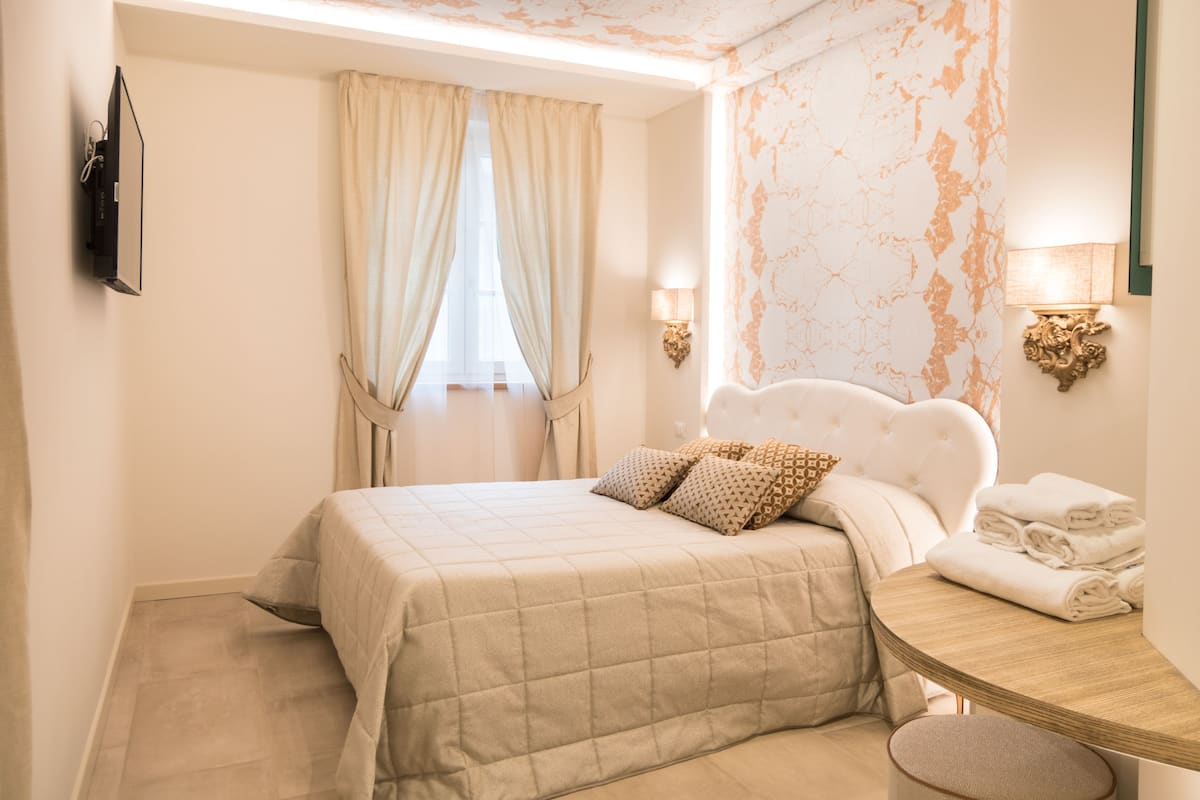 Quarto com cama, cortinas, arandelas de parede e mesa de cabeceira com toalhas.