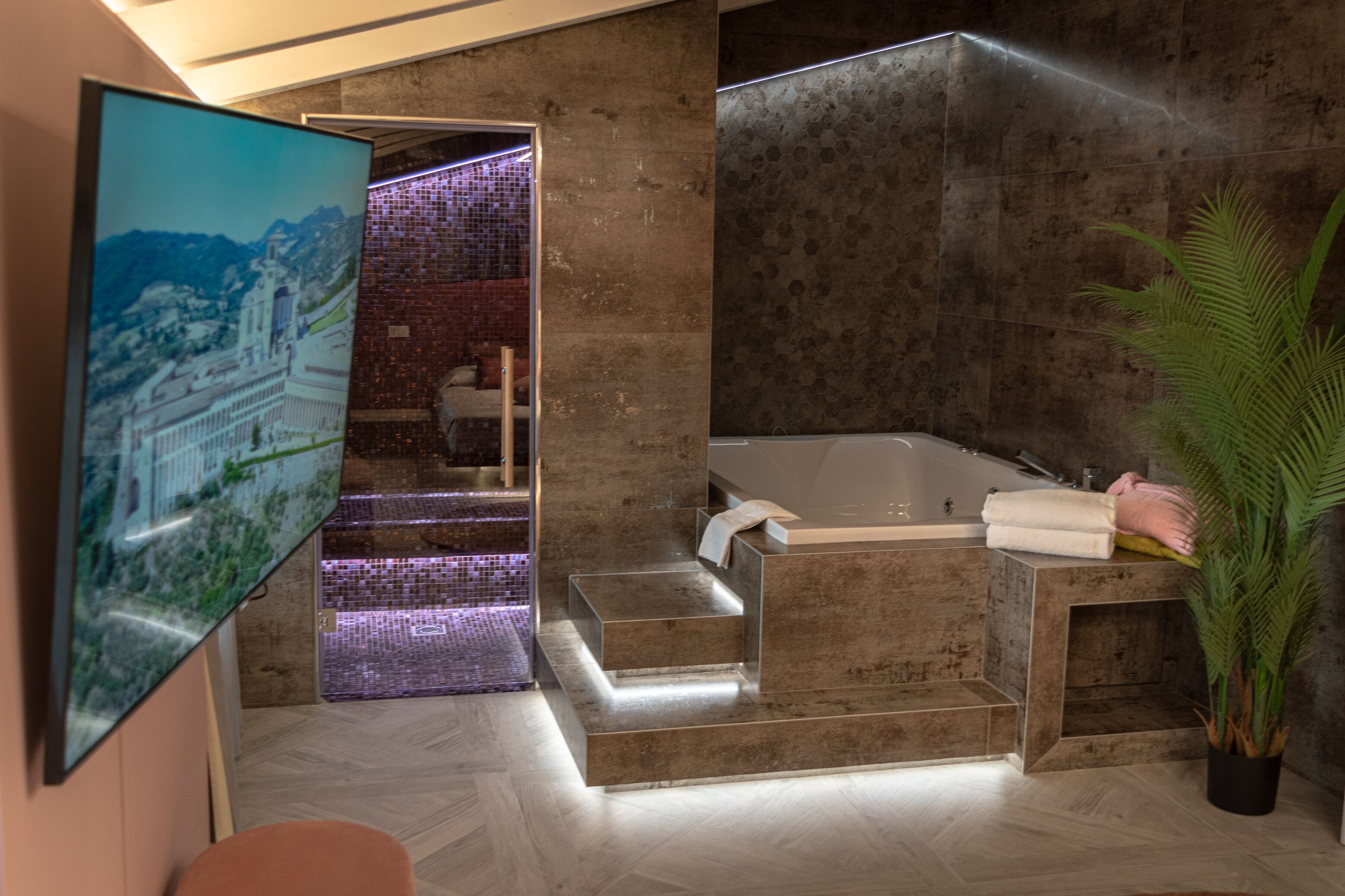 Une salle de bain moderne dotée d’une grande baignoire, d’un espace douche et d’un escalier apparent menant à un balcon.