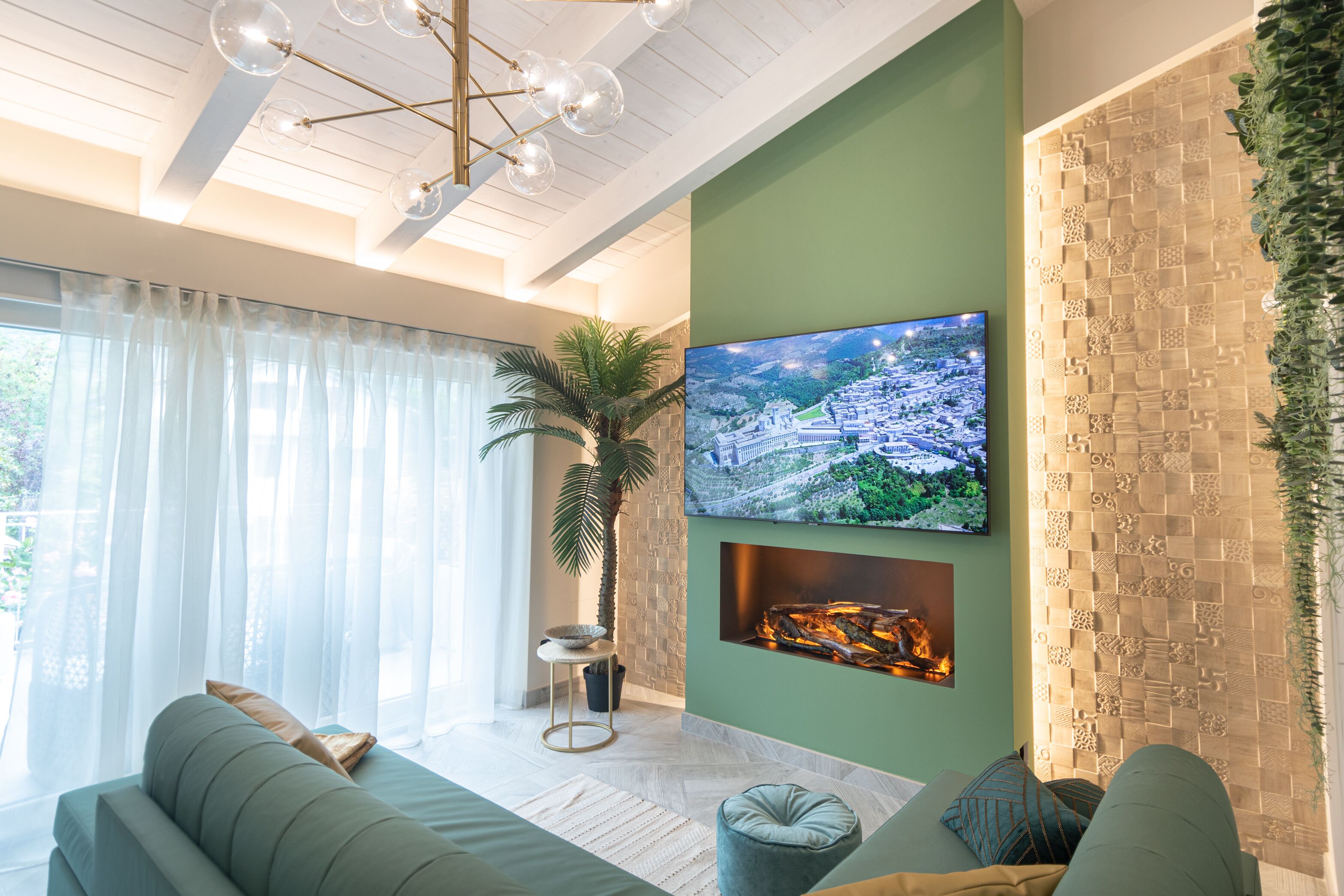 A modern living room with a large flat-screen TV mounted on a green wall, a fireplace, a sofa, and a potted plant.