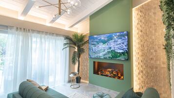 A modern living room with a large flat-screen TV mounted on a green wall, a fireplace, a sofa, and a potted plant.
