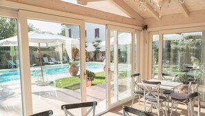 A sunlit patio with a pool, outdoor seating, and a view of the backyard.