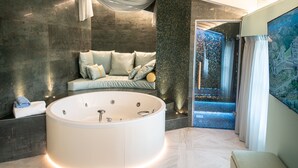 A modern bathroom with a large bathtub, a seating area with cushions, and a view of an outdoor space.