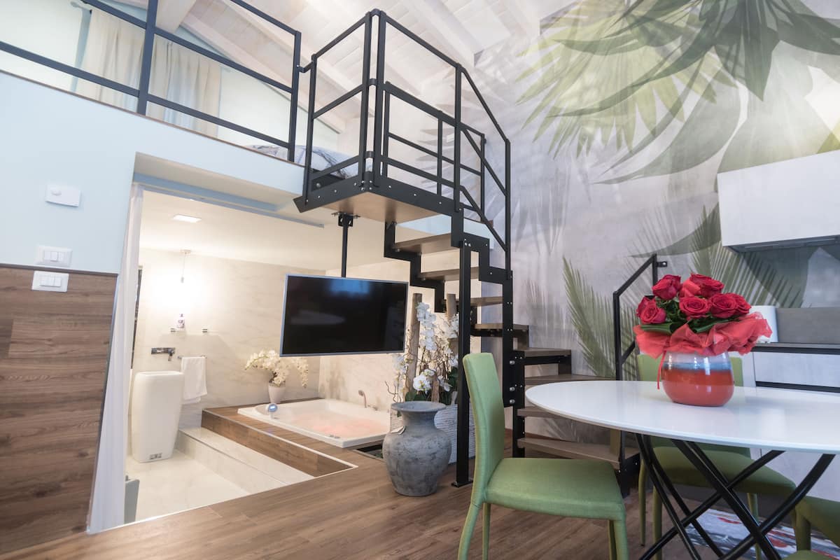 Um interior moderno com uma escada, uma televisão de tela plana, uma mesa redonda com um vaso de flores e uma planta grande.