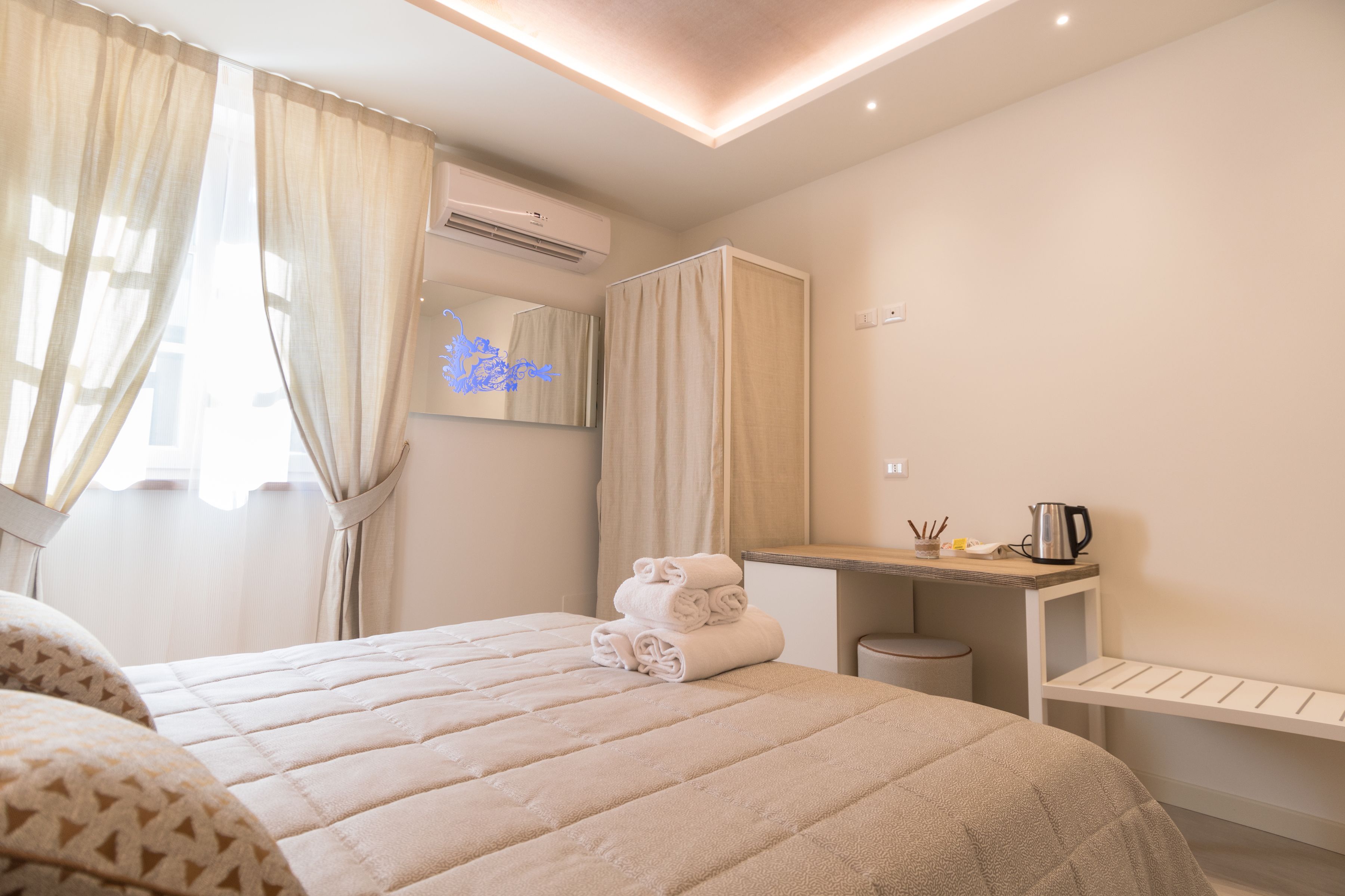 Una habitación de hotel moderna con una cama bien hecha, un escritorio con hervidor y un espejo.