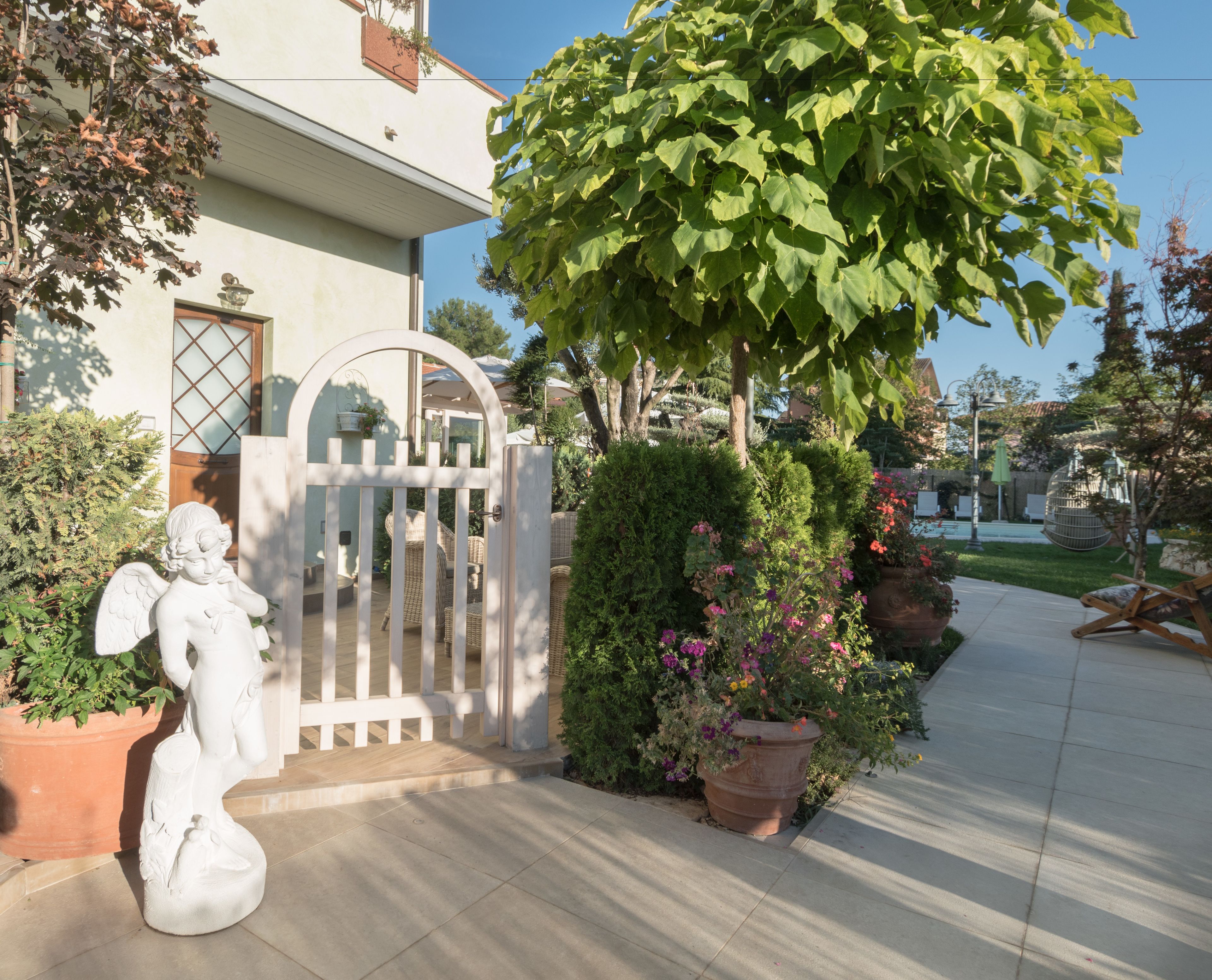 A gated entrance with a white fence, a statue of an angel, and potted plants.