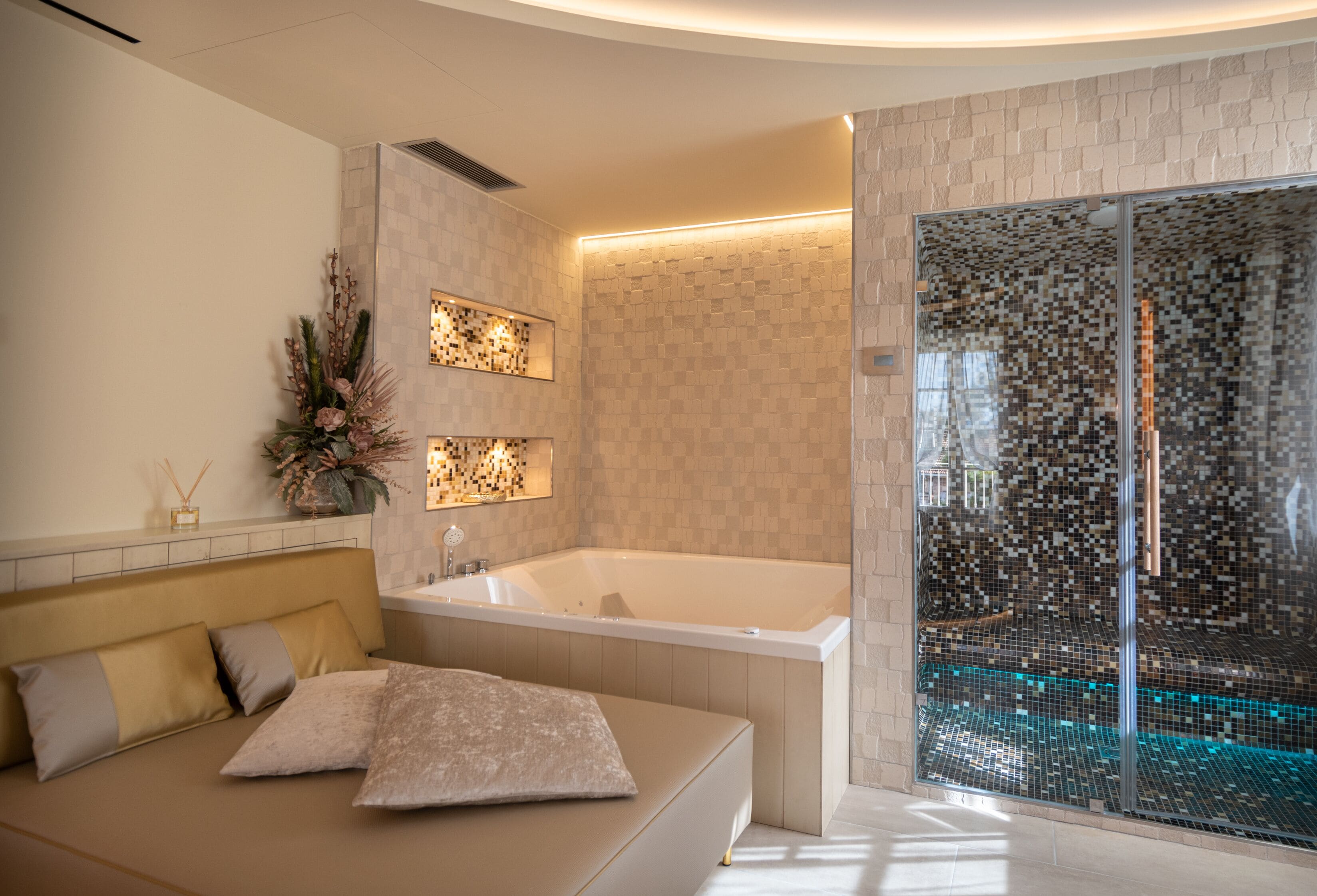 Un baño moderno con bañera, ducha envuelta en vidrio y una zona de estar con cojines.