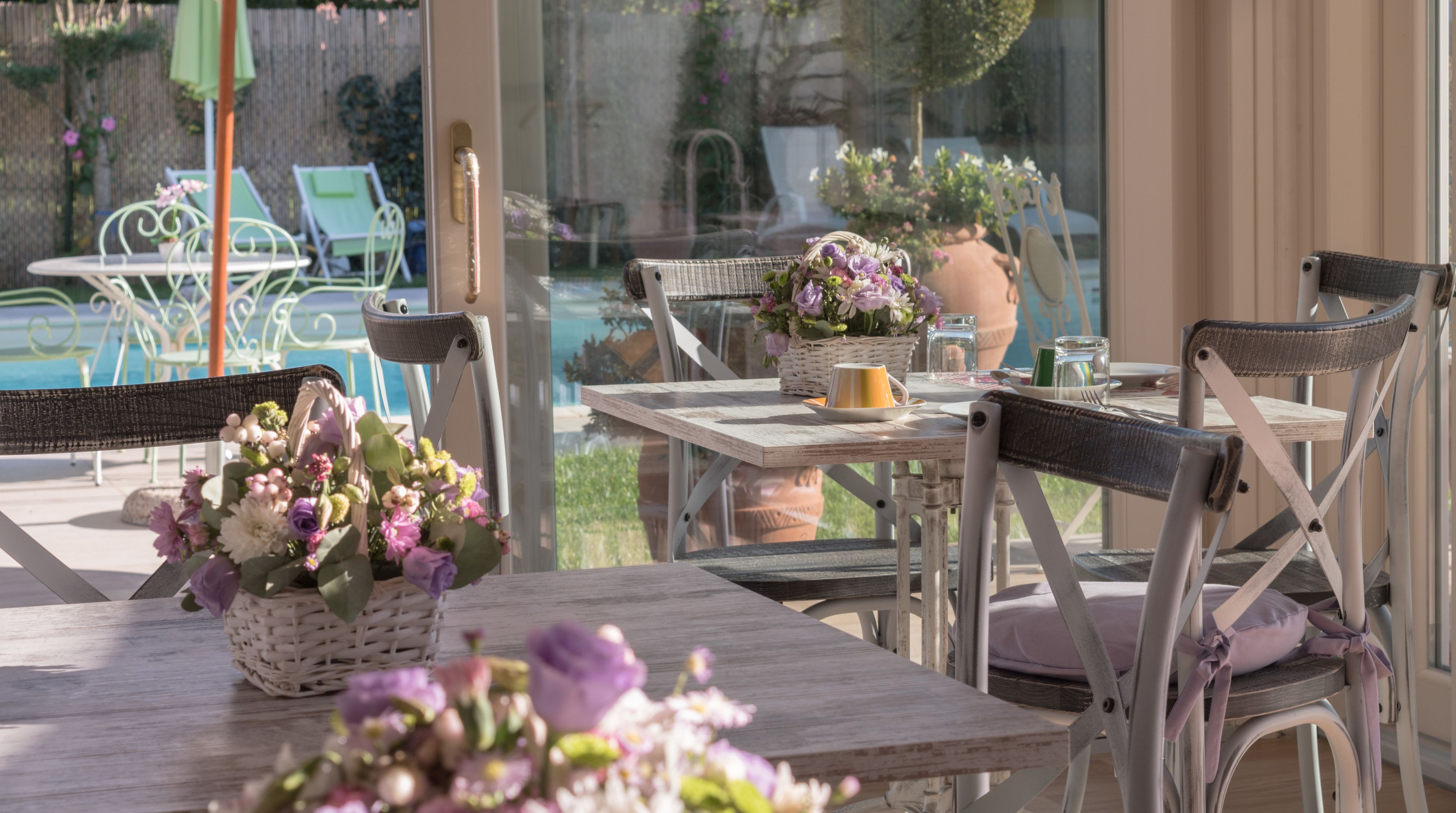 An outdoor patio with wicker chairs, a table with a vase of flowers, and a view of a pool and garden.
