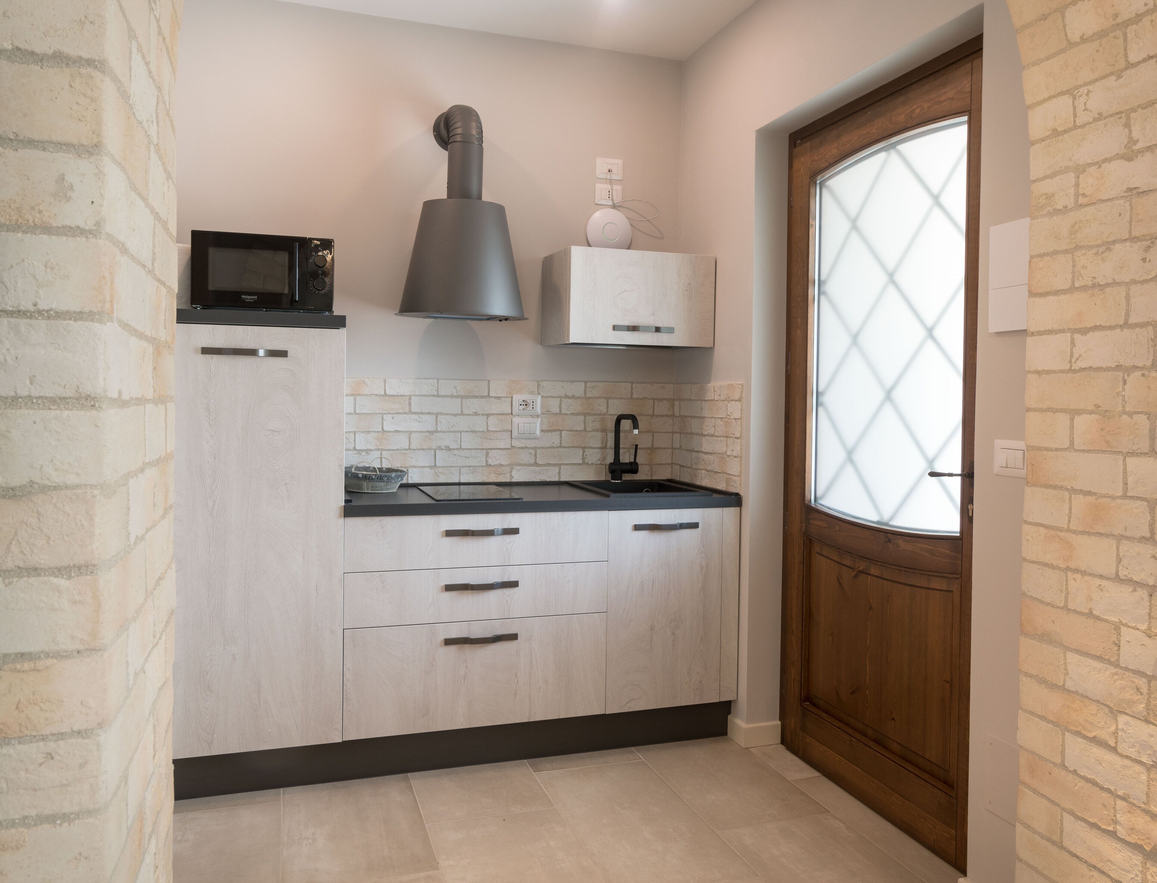 A modern kitchen with light wood cabinets, a black countertop, and a window with a diamond pattern.