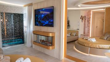 Una camera d'albergo moderna con una grande televisione, un acquario in vetro, un letto rotondo e un'area salotto separata.