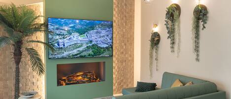 A modern living room with a green sofa, a flat-screen TV, a fireplace, and decorative wall plants.