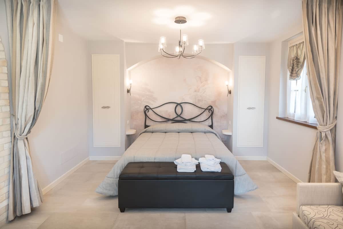 Um quarto com cama, lustre, cortinas e janela.