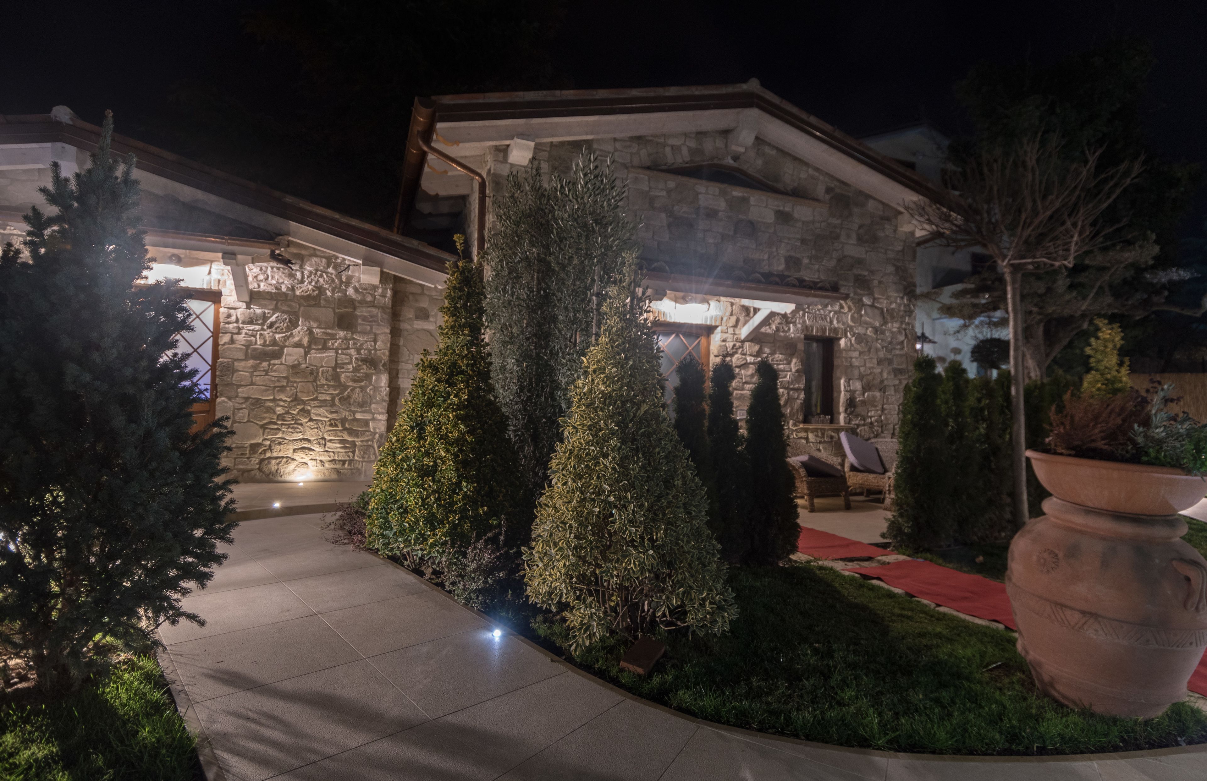 A stone building with a well-lit entrance, a paved pathway, and a large planter.