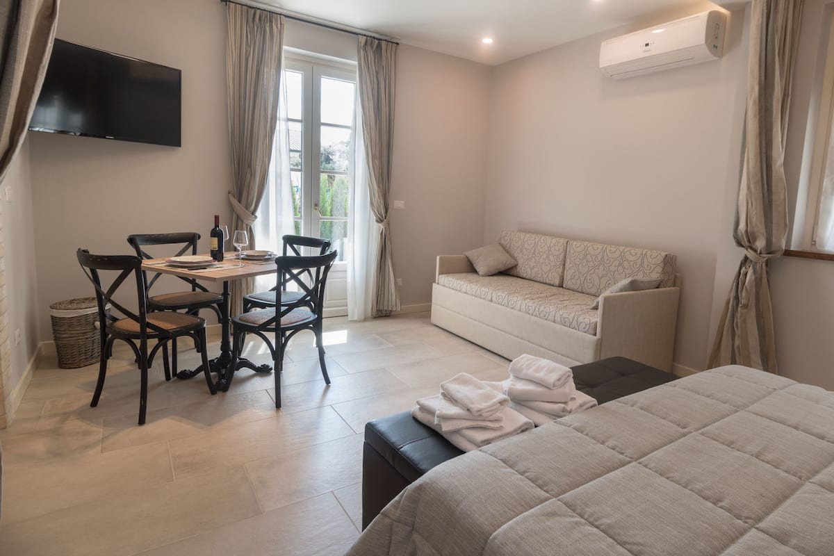 Quarto de hotel com cama, sofá, mesa de jantar com cadeiras, televisão na parede e ar condicionado.