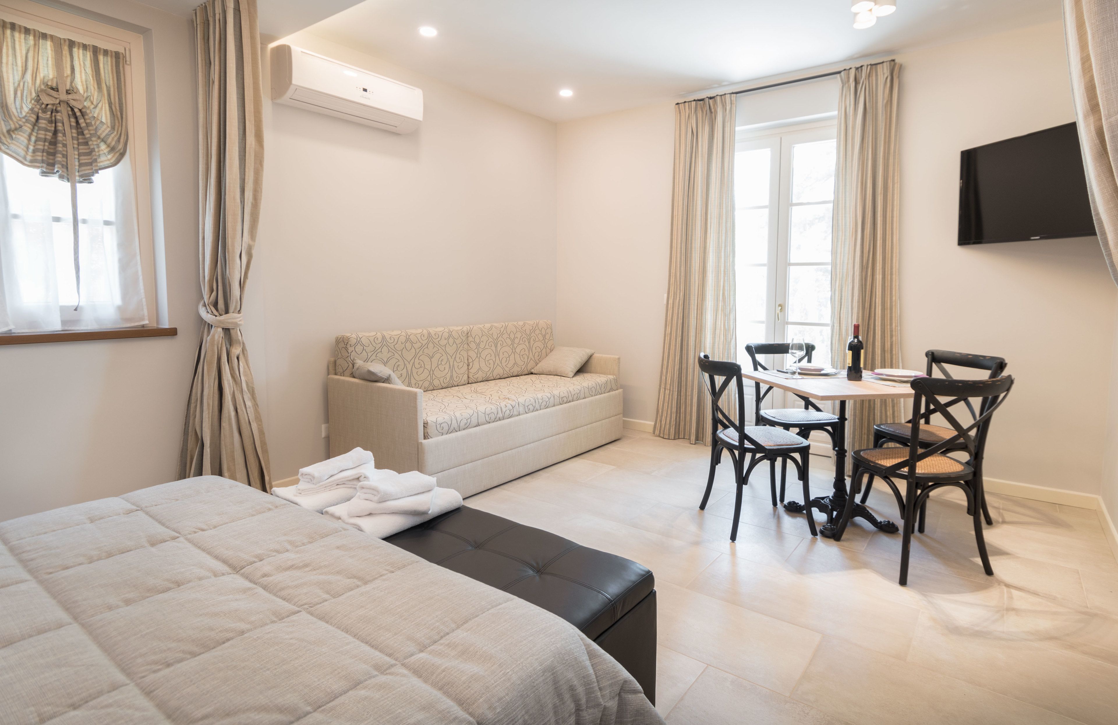 Une chambre d’hôtel comprenant un lit, un canapé, une table à manger avec des chaises et un téléviseur fixé au mur.