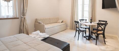 A hotel room with a bed, a sofa, a dining table with chairs, and a TV mounted on the wall.