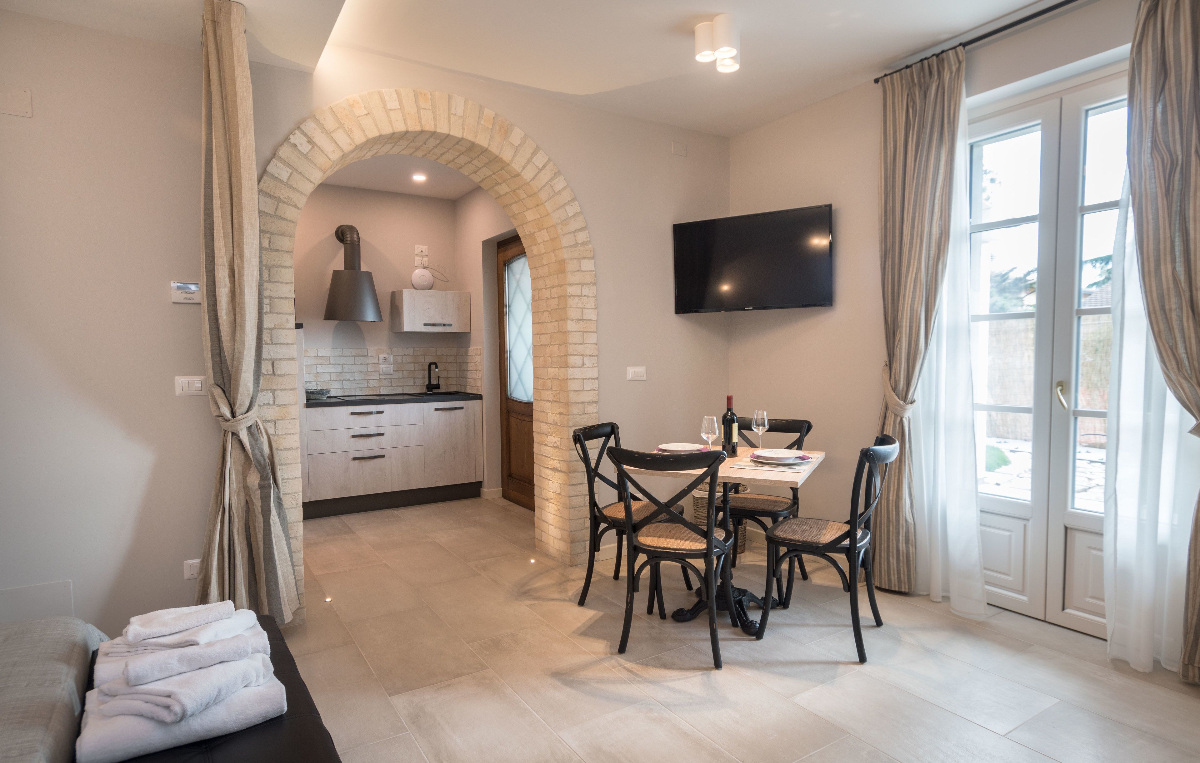 A modern hotel room with a kitchen, dining area, and a large window with curtains.