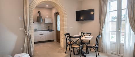 A modern hotel room with a kitchen, dining area, and a large window with curtains.