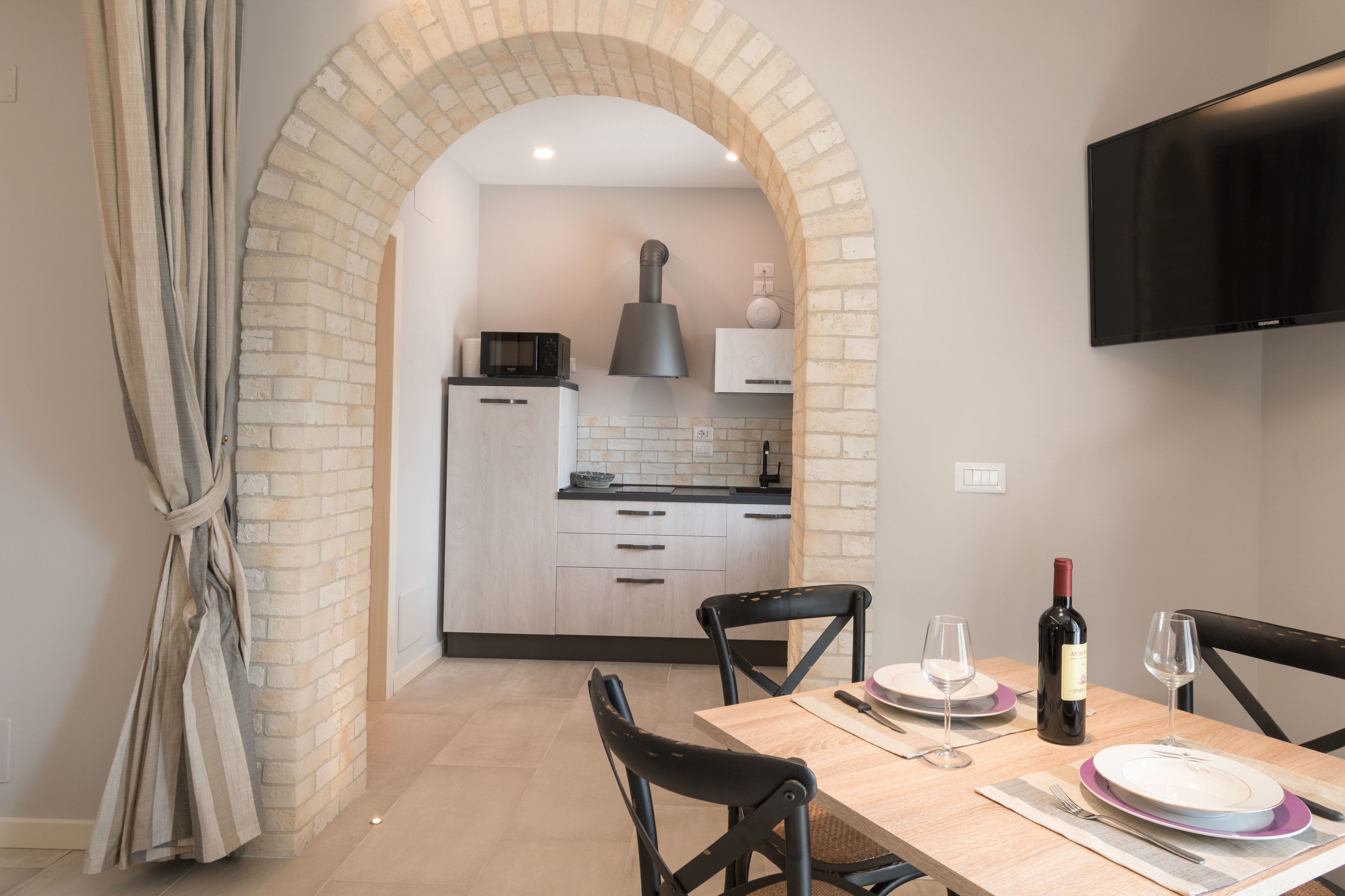 A dining area with a table set for two, a wine bottle, and a TV mounted on the wall.