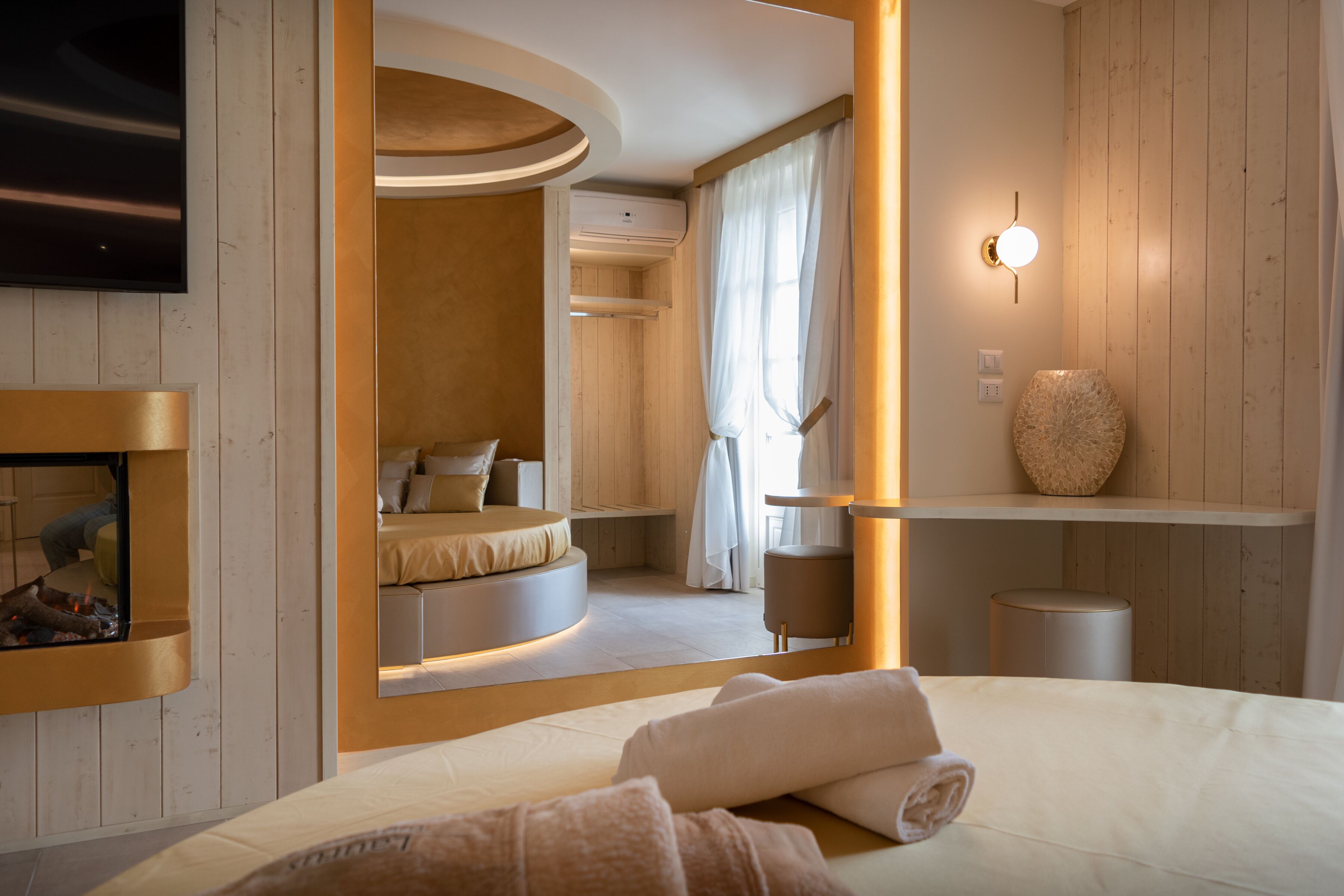 A modern bedroom with a circular bed, a fireplace, and a large mirror.