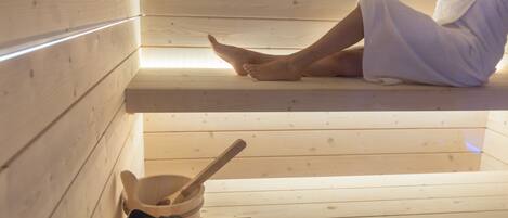 A wooden sauna with a person sitting on a bench, a wooden bowl, and a wooden spoon.