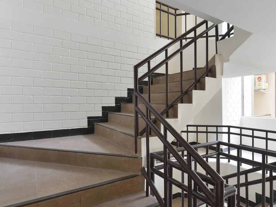 Una escalera moderna con barandilla de metal, paredes de ladrillo blanco y suelo pulido.