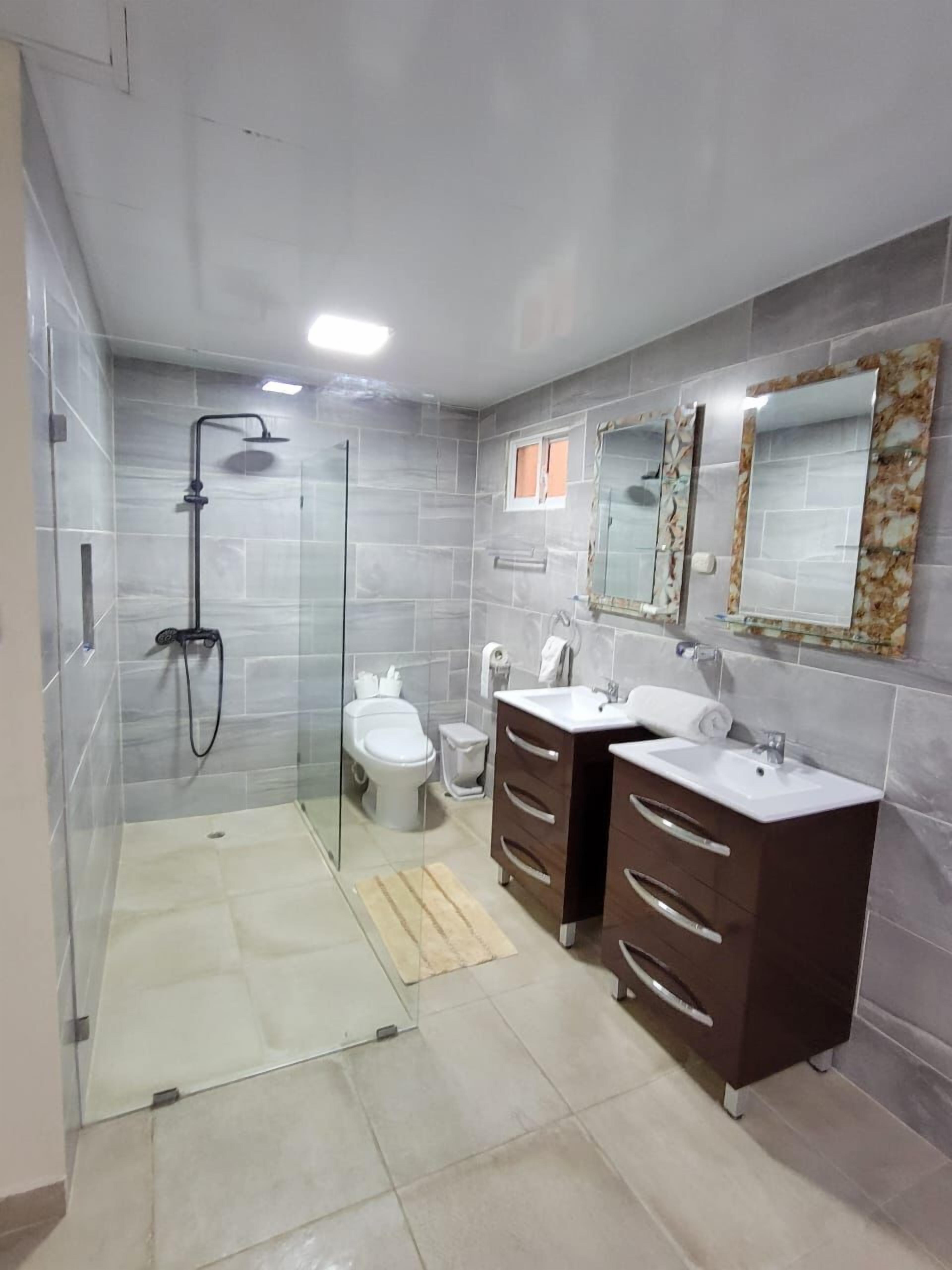 A modern bathroom with a glass-enclosed shower, a toilet, and two sinks with dark cabinets.