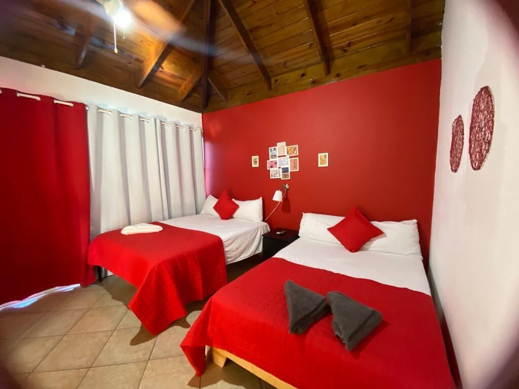 A room with two beds, red curtains, a wooden ceiling, and a wall with pictures.