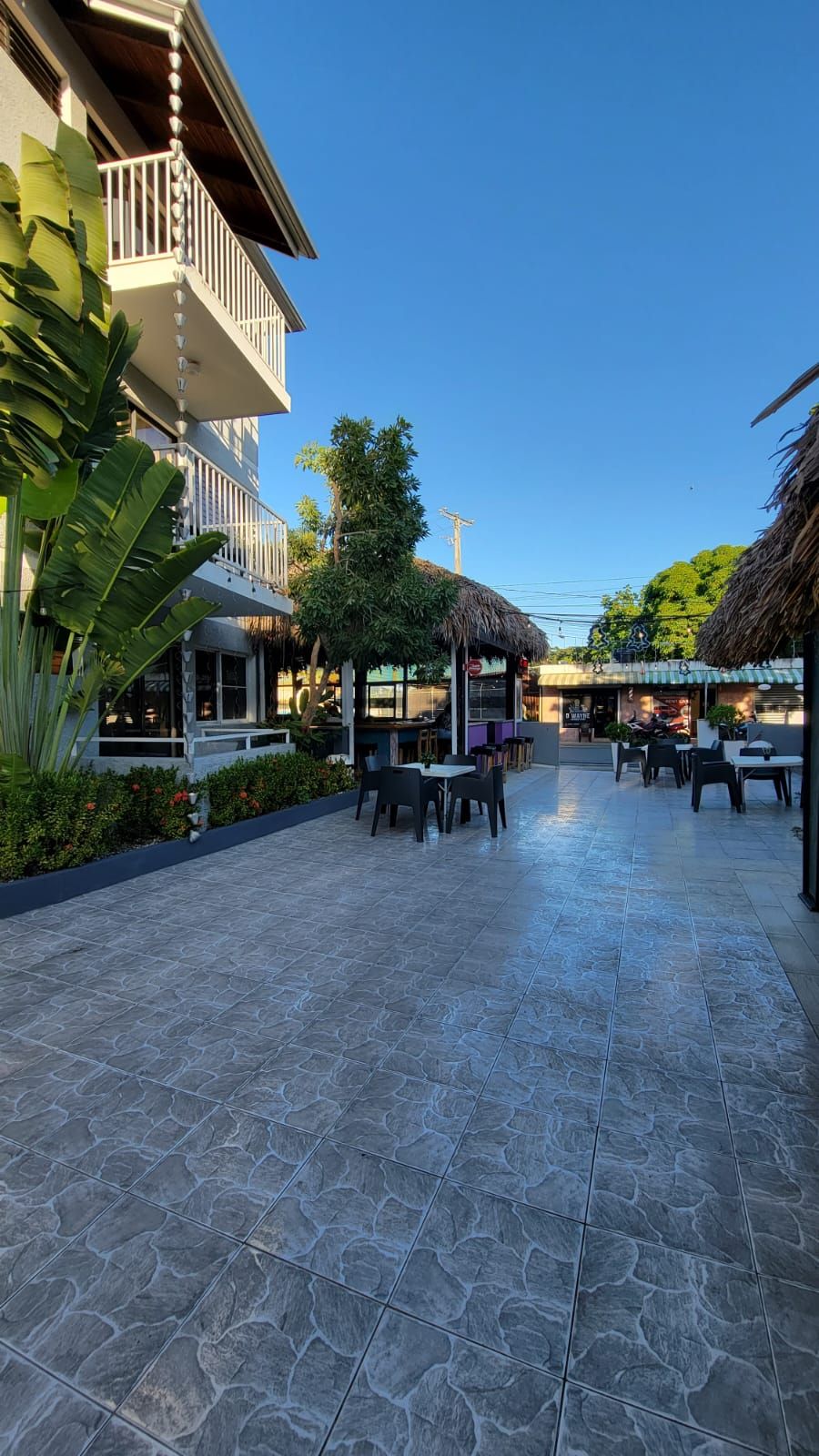An outdoor patio area with tables and chairs, surrounded by buildings and vegetation.