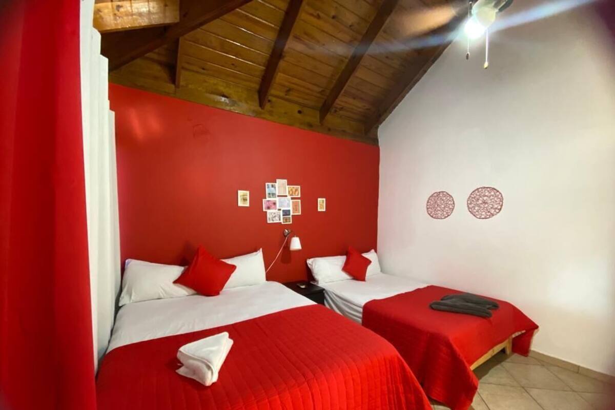 Ein Zimmer mit zwei Betten, roter Bettwäsche, einer Holzbalkendecke und einer Wand mit Bildern und einer Dekoration.