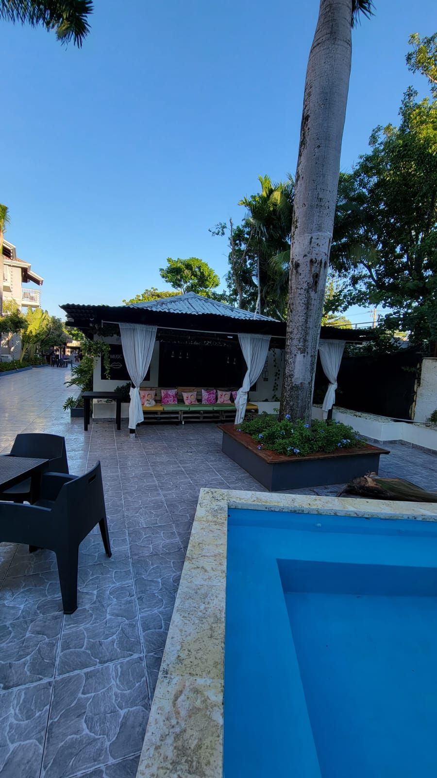 A poolside area with a covered seating area, a pool, and outdoor furniture.