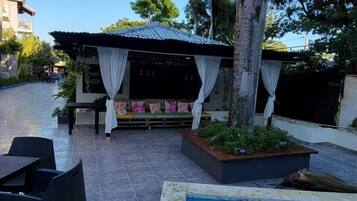A poolside area with a covered seating area, a pool, and outdoor furniture.