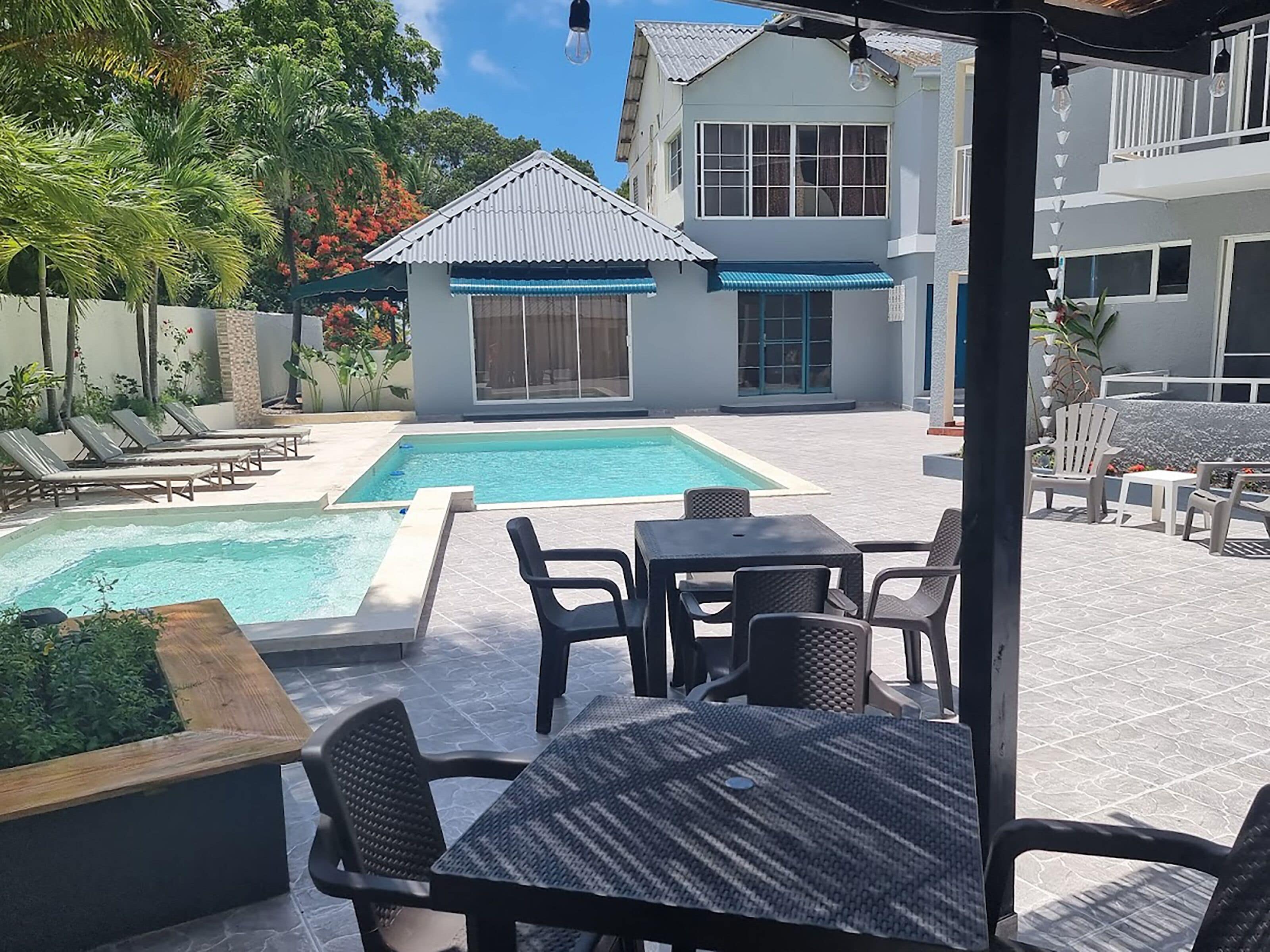 Un espace piscine comprenant des chaises longues, une table et un coin salon abrité.