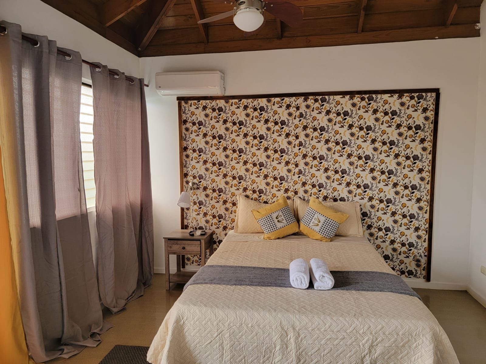 A bedroom with a bed, curtains, a nightstand, and a wall-mounted air conditioner.
