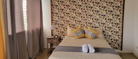 A bedroom with a bed, curtains, a nightstand, and a wall-mounted air conditioner.