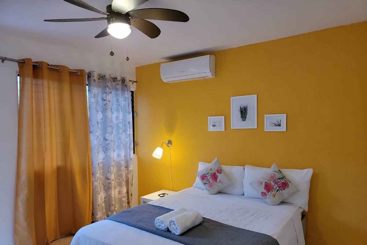 Ein Hotelzimmer mit Bett, Deckenventilator, Klimaanlage und Nachttisch mit Lampe.