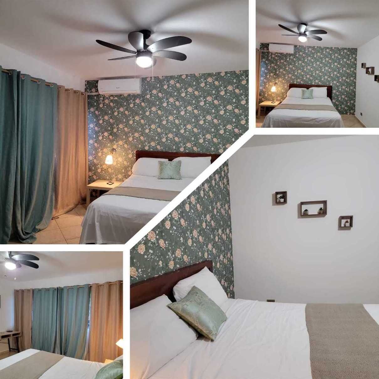 A hotel room with a bed, curtains, a ceiling fan, and a floral wallpaper.