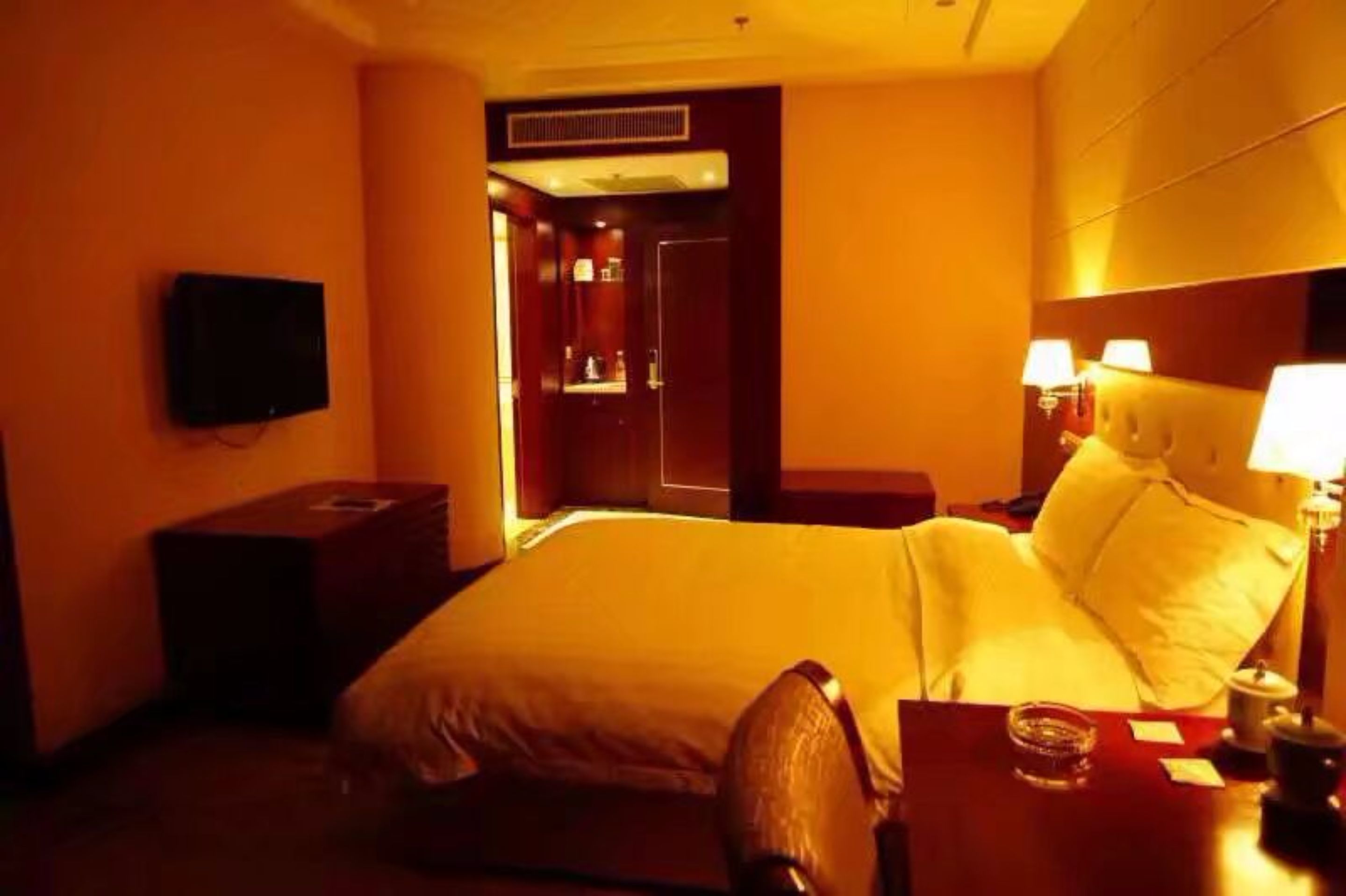A hotel room with a bed, bedside tables, a TV, and a mirror.