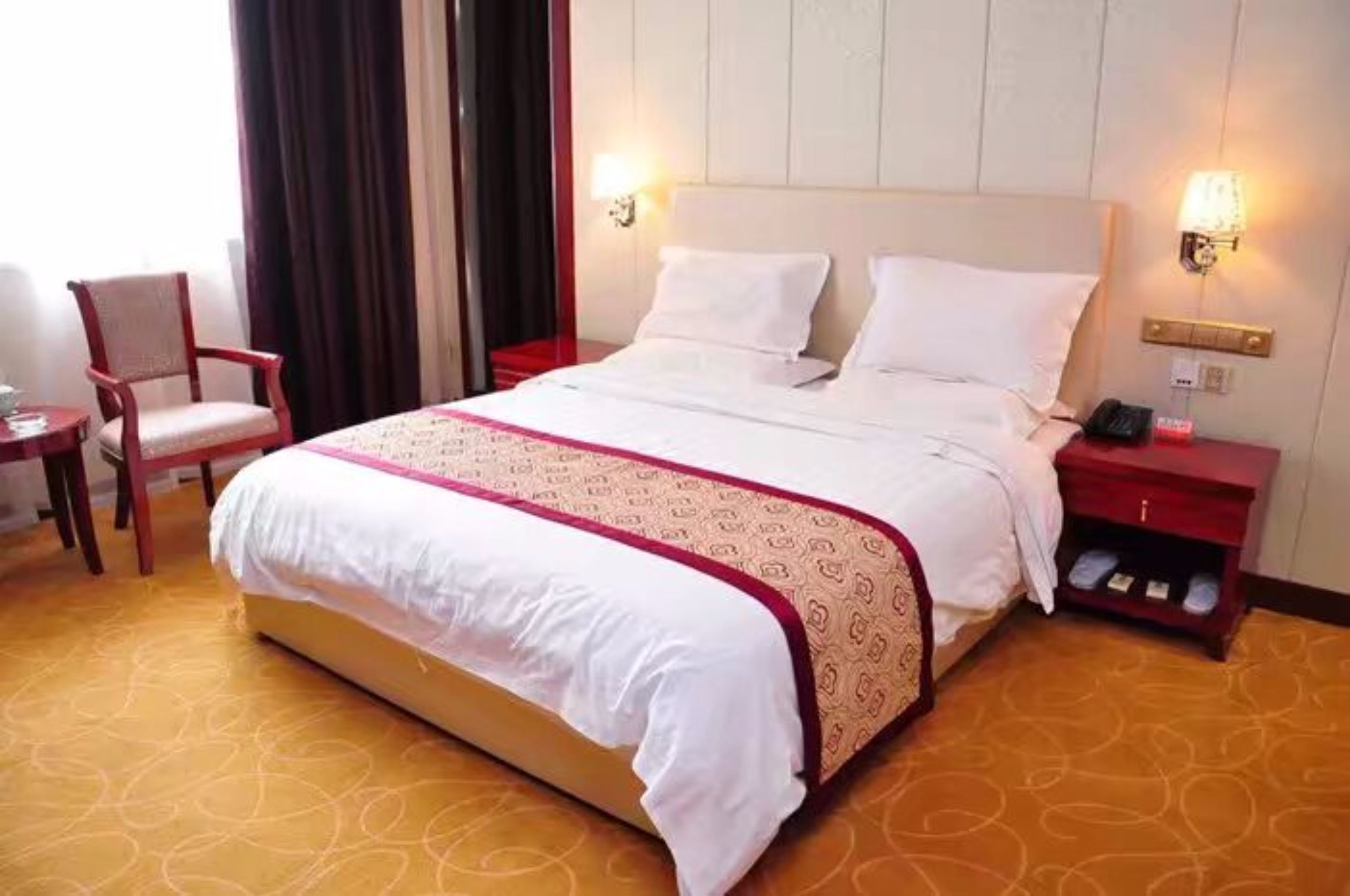 Una habitación de hotel con una cama grande, una mesita de noche, una silla y una lámpara.