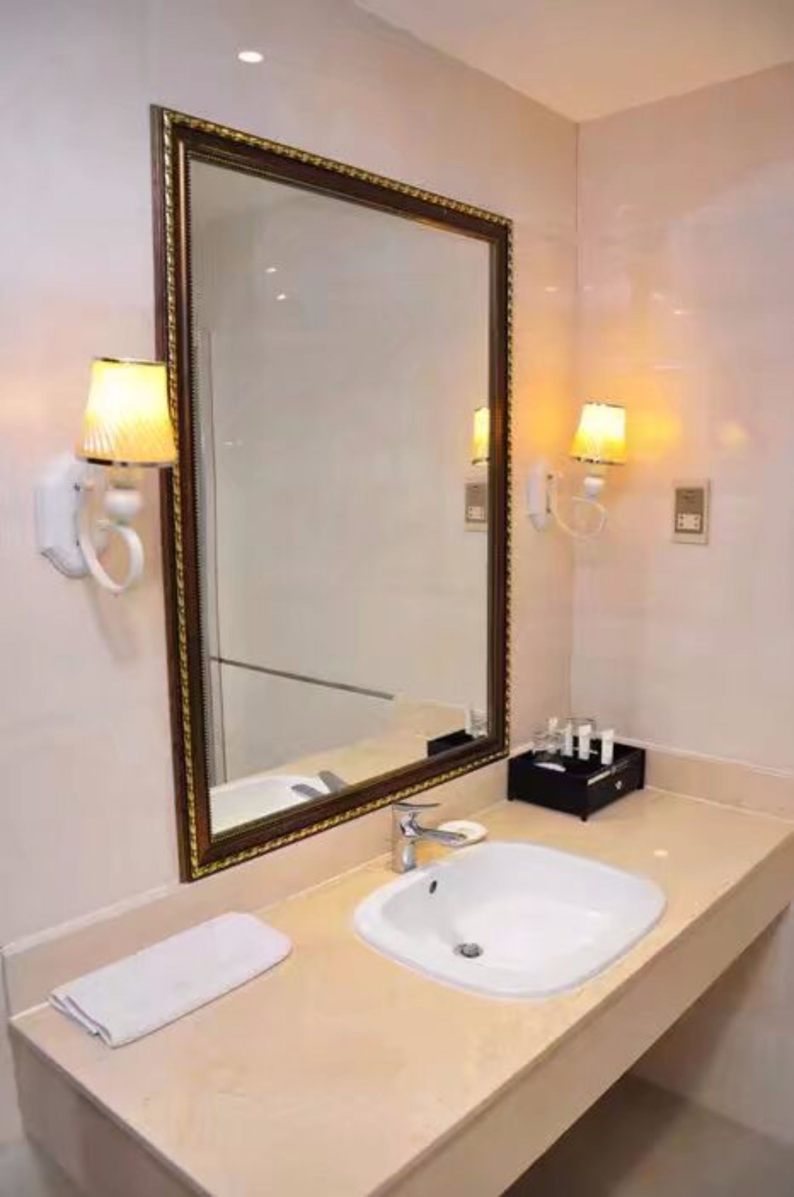 Een hotelbadkamer met een grote spiegel, een wastafel en twee wandlampen.