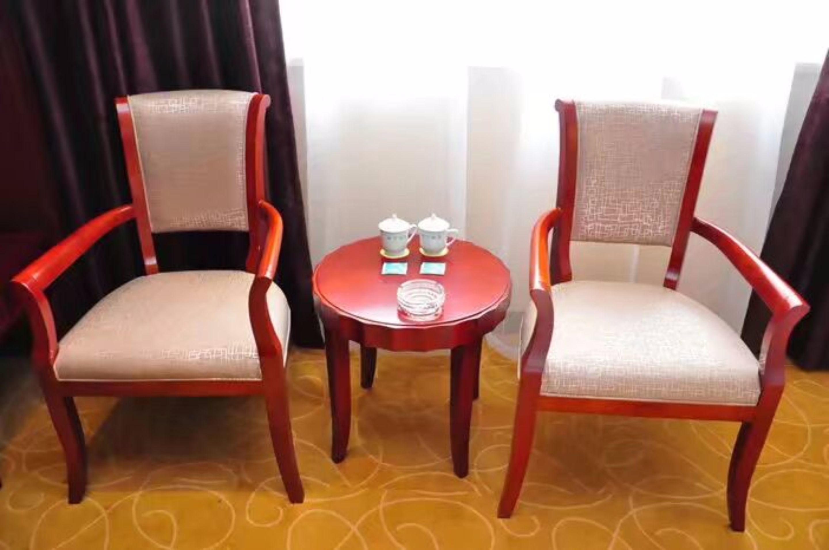Two wooden chairs with cushioned seats and backs, a small round table with two teapots and a coiled white cable, and a patterned carpet.