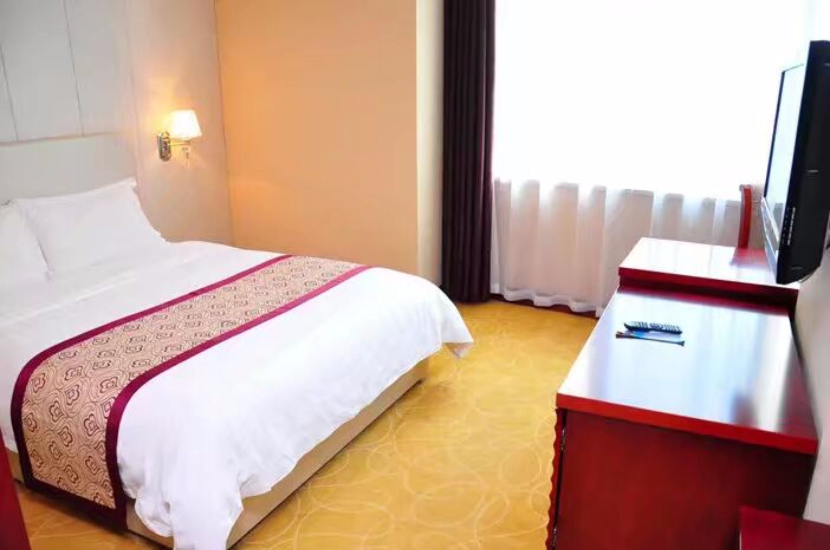 Habitación de hotel con cama, escritorio, televisor y ventana con cortinas.