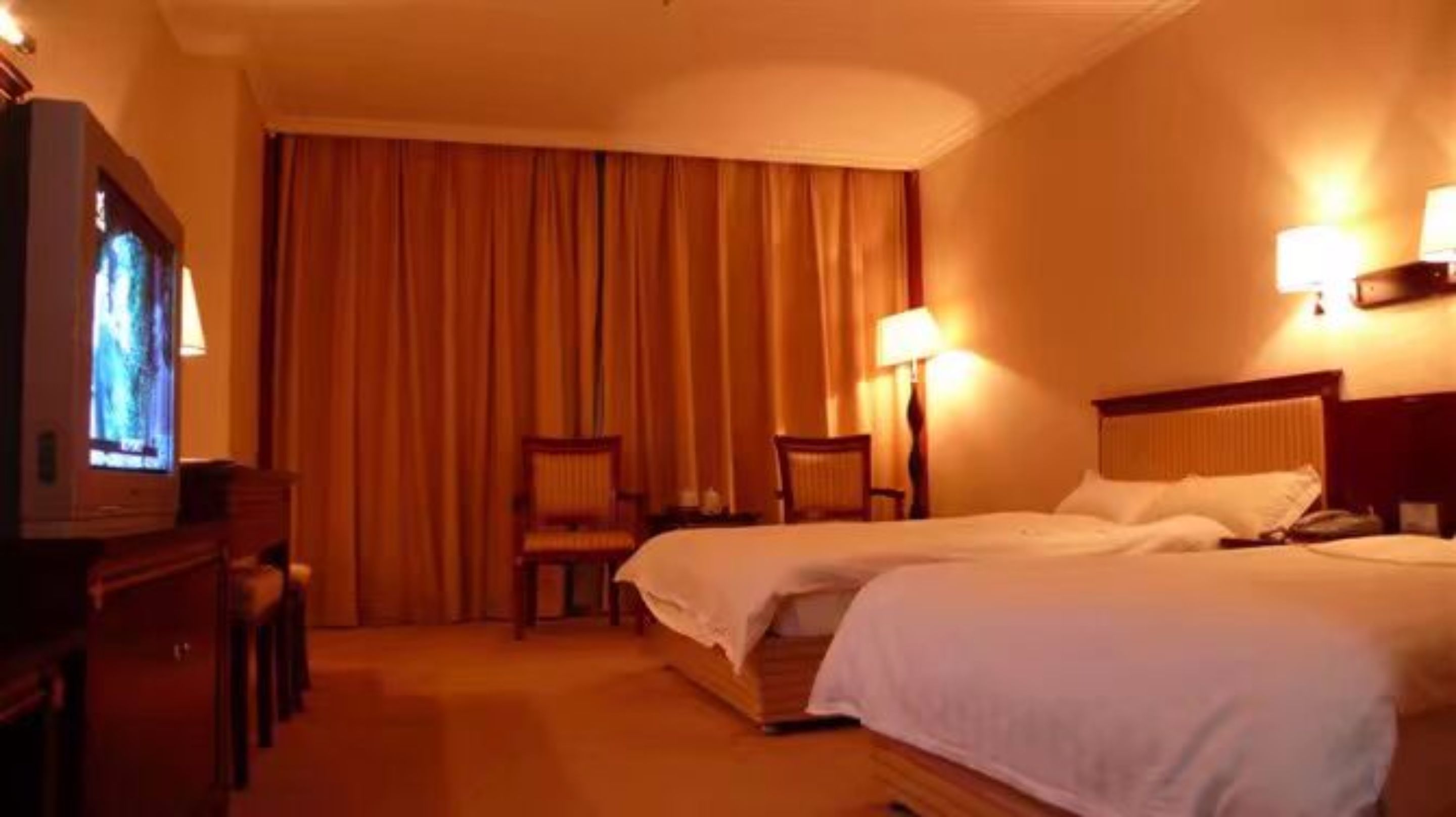 A hotel room with two beds, a television, a desk, and two chairs.