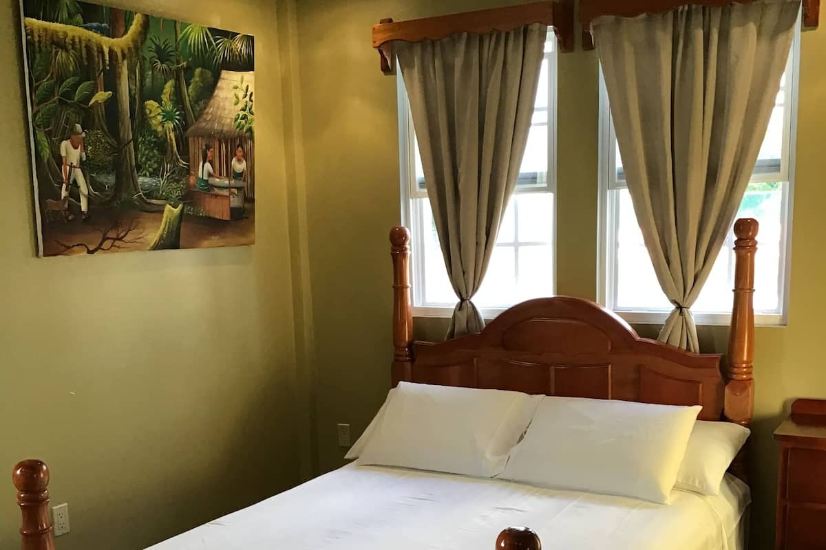 Un dormitorio con cama de madera, cortinas color beige y un cuadro de una escena selvática en la pared.