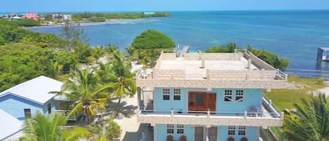 Uma casa de dois andares com varanda, cercada por vegetação exuberante e vista para o oceano.