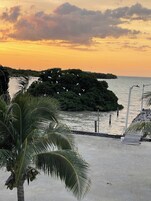 Una playa con una pequeña isla, palmeras y un paseo de madera.