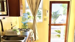 A kitchen with a sink, stove, and microwave. There is a water dispenser and a window with curtains. An exit door is visible.